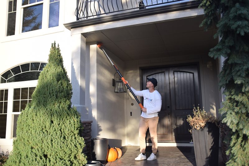 Brushing spider webs off a porch ceiling with a long-handled web brush